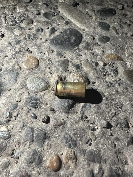 A bullet casing from what appears to be a pistol-style weapon lies discarded on the sidewalk.